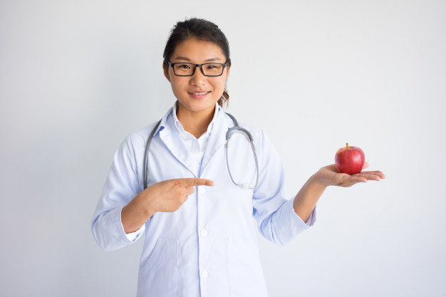 Una giovane dottoressa in camice bianco con una mela nel palmo della mano